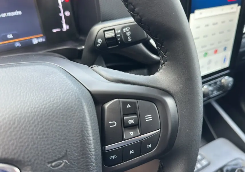 Gros plan sur le volant cuir multifonctions du Ford Ranger gris iconic, avec commandes intégrées et écran tactile en arrière-plan.