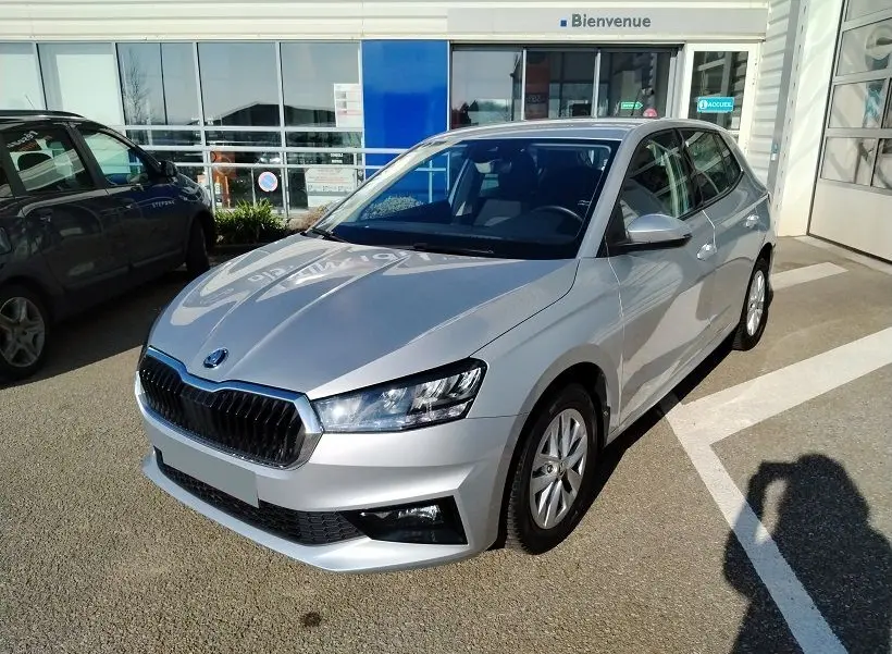 Vue 3/4 avant droite d'une Skoda Fabia blanche 2023, avec calandre noire et phares LED, stationnée devant un bâtiment.