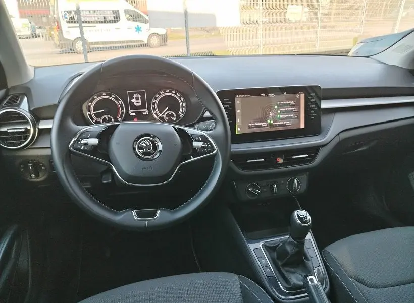 Vue intérieure frontale du poste de conduite d'une Skoda Fabia blanche 2023 avec volant multifonction et écran tactile central.