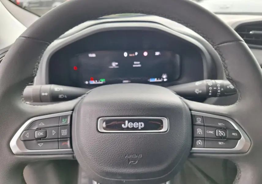 Vue rapprochée du volant Jeep Renegade 2024, noir avec commandes intégrées et tableau de bord numérique flou.