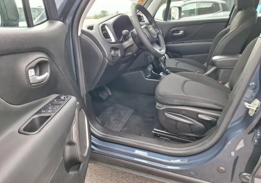 Vue intérieure côté conducteur d'un Jeep Renegade bleu 2024, montrant sièges noirs et accoudoir central.
