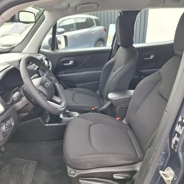 Vue intérieure côté conducteur du Jeep Renegade bleu 2024, sièges noirs avec accoudoir central et volant multifonction.