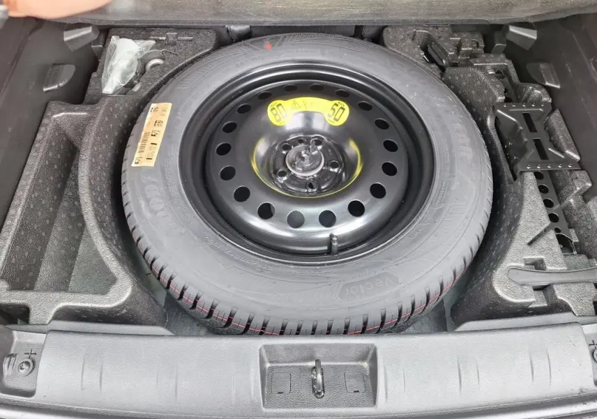 Vue de dessus sur la roue de secours noire dans le coffre du Jeep Renegade bleu 2024, avec outils de bord rangés.