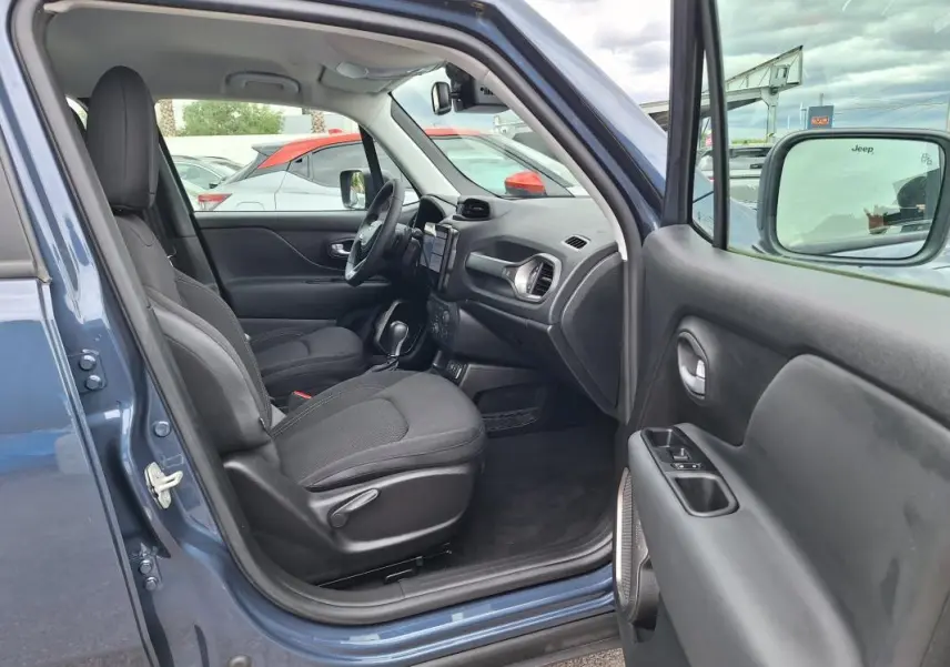 Vue intérieure côté conducteur d'un Jeep Renegade bleu 2024, montrant sièges noirs et tableau de bord avec écran tactile.