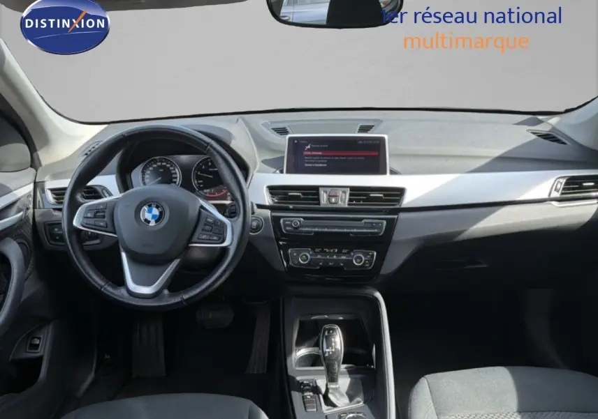 Vue intérieure avant du BMW X1 blanc 2022, mettant en valeur le tableau de bord moderne et le volant multifonction.