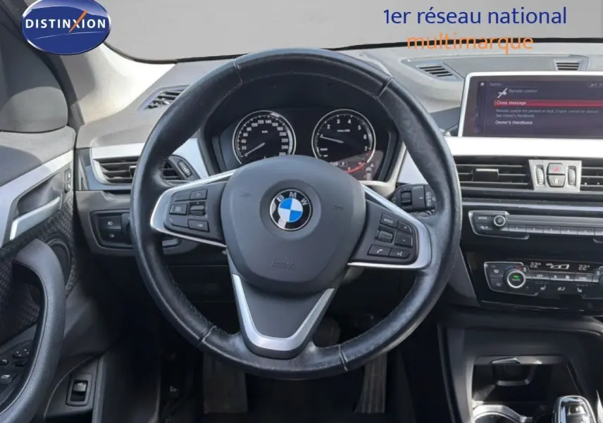 Vue intérieure centrée sur le volant noir d'une BMW X1 2022, avec tableau de bord et écran multimédia visibles.