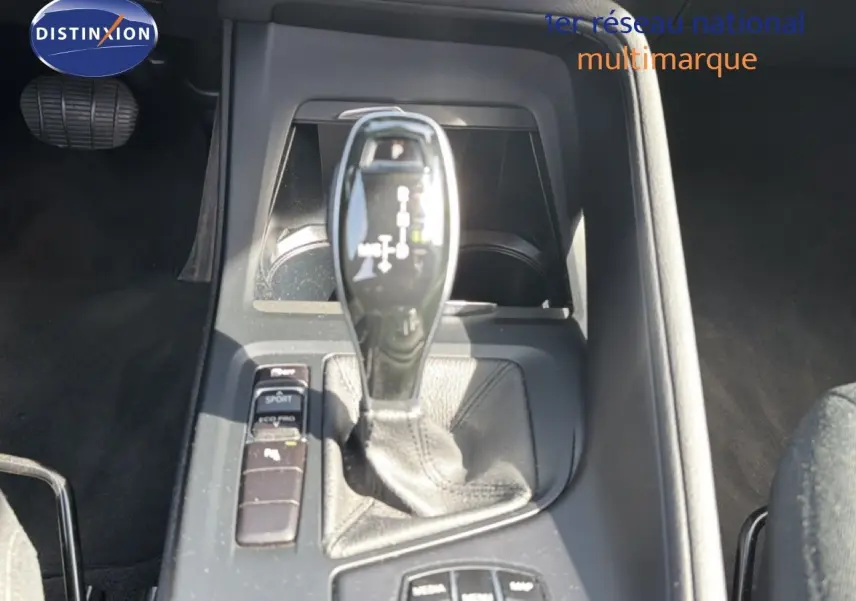 Gros plan sur la console centrale et levier de vitesse automatique d’une BMW X1 blanche, intérieur noir.