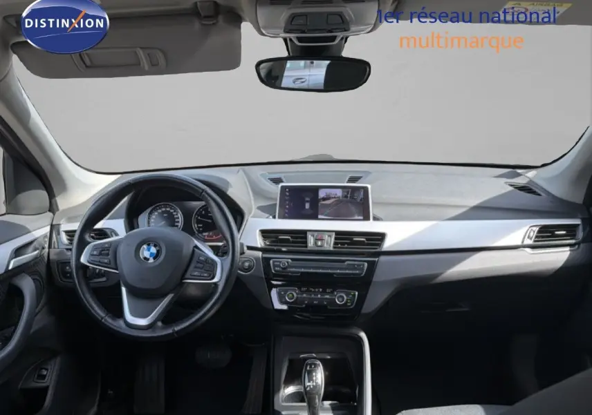 Vue intérieure avant de la BMW X1 blanche 2022, tableau de bord moderne avec écran central et volant multifonction.