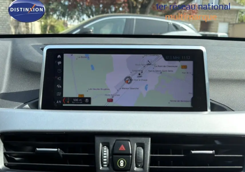 Écran tactile central affichant la navigation GPS dans l'habitacle d'un BMW X1 blanc, vue intérieure frontale.