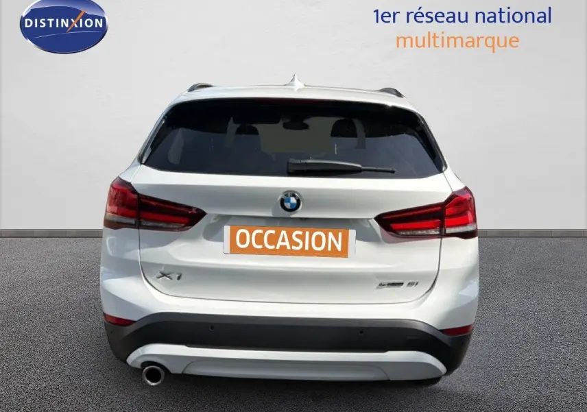 Vue arrière d’un BMW X1 blanc de 2022 avec feux rouges et plaque « OCCASION » visible sur un fond neutre.