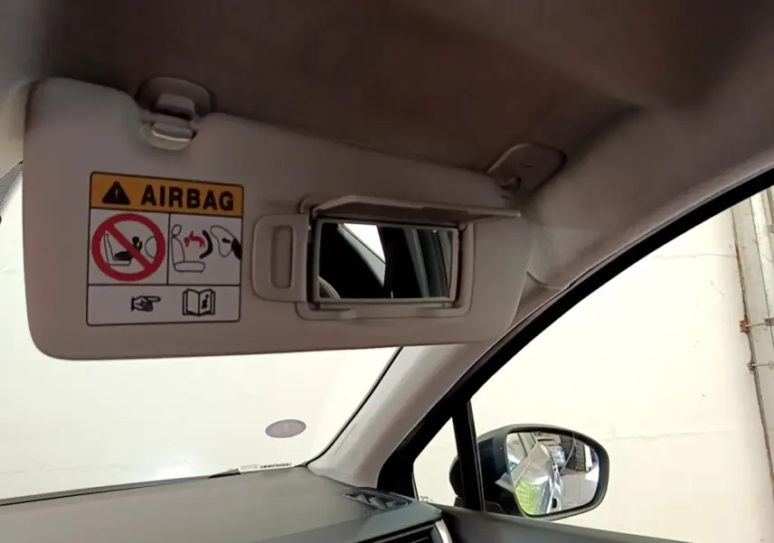 Détail intérieur du pare-soleil côté conducteur avec miroir et avertissement airbag, rétroviseur extérieur noir visible.