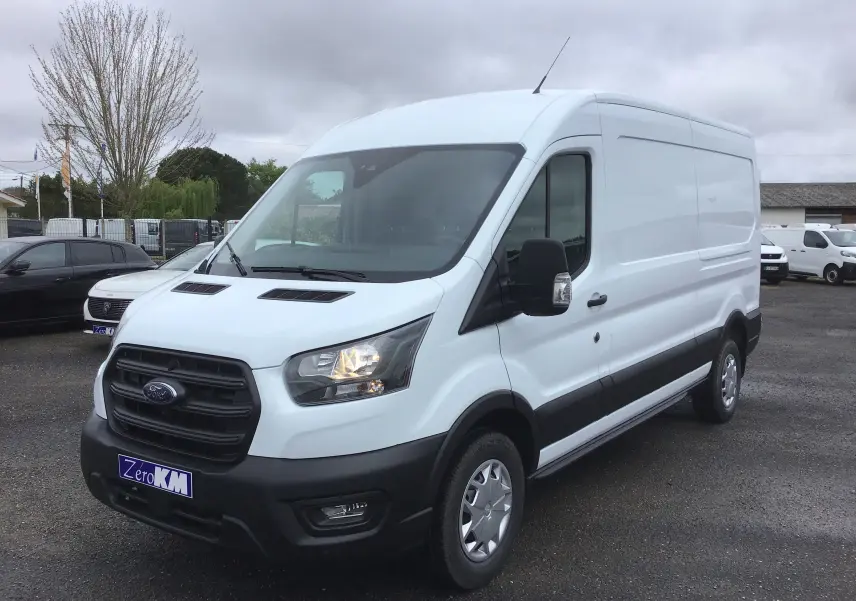 Fourgon blanc Ford Transit 350 L3H2 vu en 3/4 avant droit avec calandre noire et phares allumés.