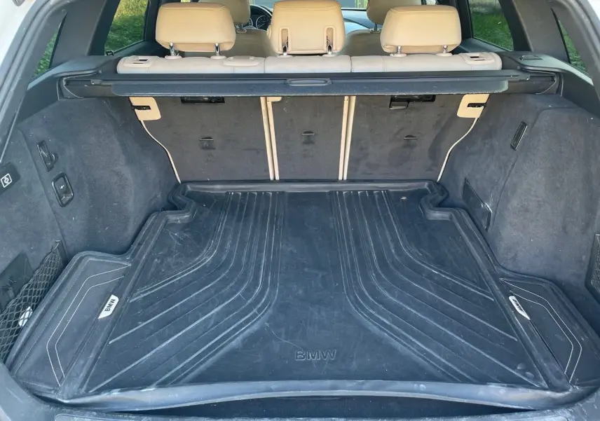 Coffre ouvert d'une BMW Série 3 Touring F31 blanc, vue arrière montrant le tapis de coffre noir avec logo BMW.