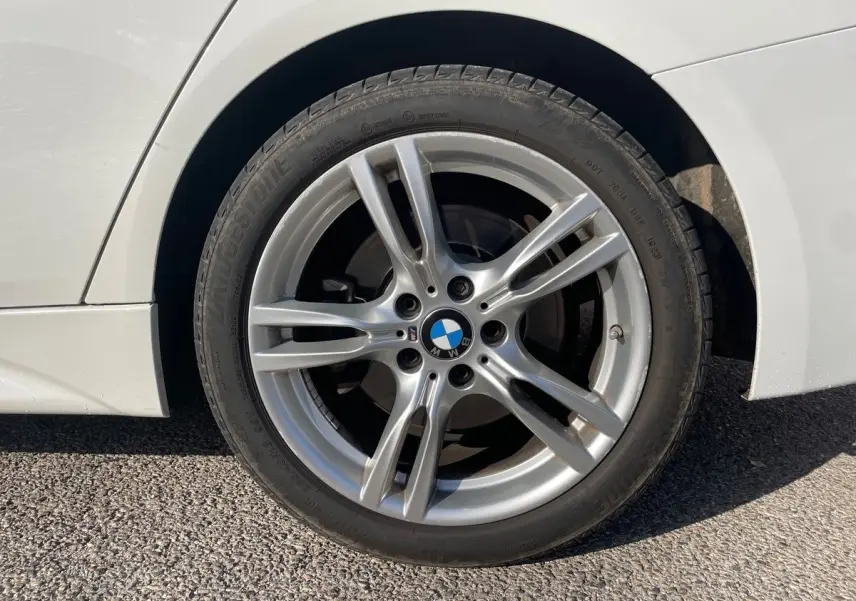 Gros plan sur la roue avant droite d'une BMW Série 3 Touring F31 blanche avec jante alliage M Sport visible.
