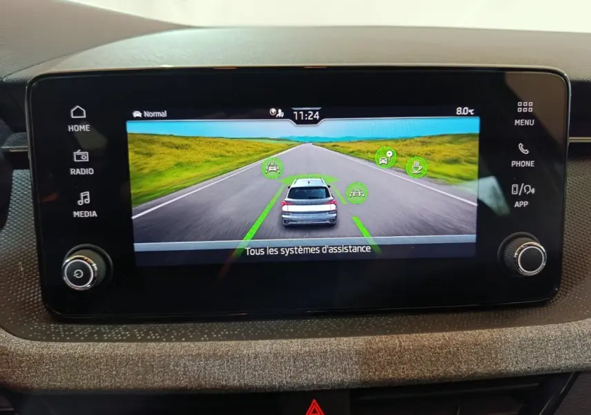 Écran tactile central affichant l’aide à la conduite avec vue arrière d’un Skoda Kamiq gris clair sur route droite.