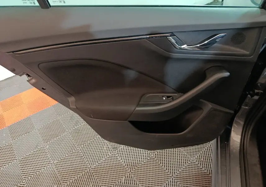 Vue rapprochée de la porte intérieure côté gauche d’un Skoda Kamiq gris clair, avec poignée chromée et commande de lève-vitre.