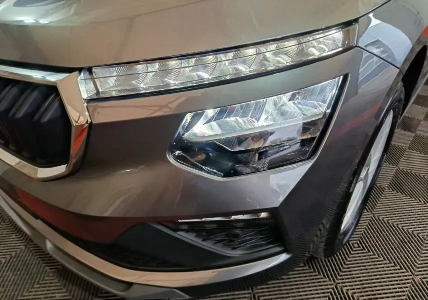 Gros plan sur le phare avant droit gris clair du Skoda Kamiq 2024 avec calandre chromée et feux LED distinctifs.