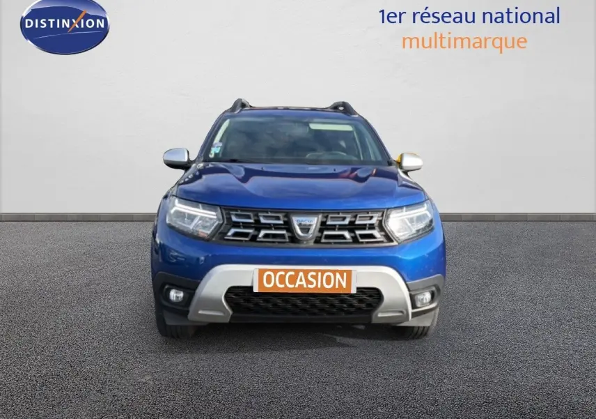 Vue frontale d'un Dacia Duster 2022 bleu Iron avec calandre chromée et plaque "OCCASION" visible.