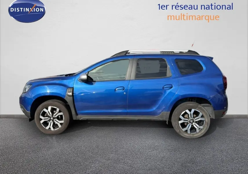 Vue latérale gauche d’un Dacia Duster 2022 bleu Iron avec jantes alliage bicolores et barres de toit.