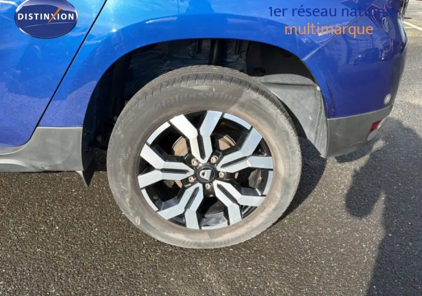 Gros plan sur la roue arrière droite du Dacia Duster bleu Iron 2022 avec jante alliage bicolore.