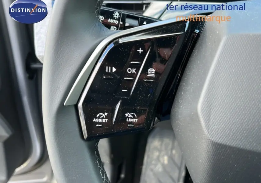 Gros plan sur les commandes noires du volant en cuir gris du Peugeot 5008 2025 hybride, côté gauche.