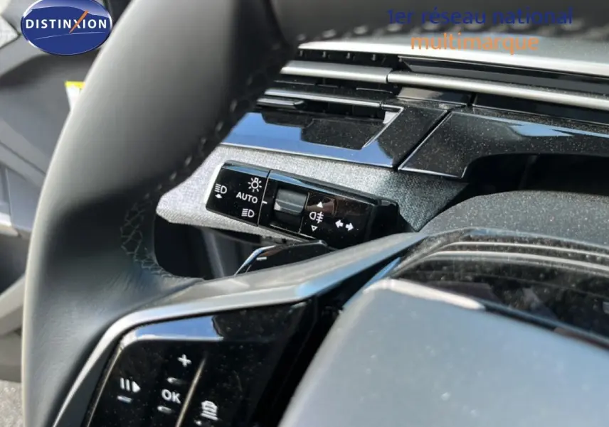 Gros plan sur le volant et la commande des phares du Peugeot 5008 1.2 Hybrid 145ch finition Allure, intérieur noir.