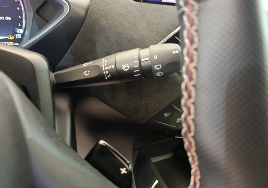 Gros plan sur la manette d’essuie-glace à gauche du volant cuir noir avec surpiqûres rouges dans un DS3 gris foncé 2024.