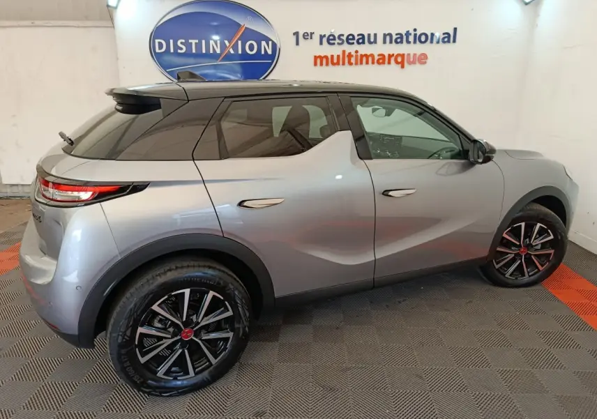 Vue latérale droite d'une DS3 2024 gris foncé avec jantes noires et toit noir, stationnée en intérieur sur sol damier.