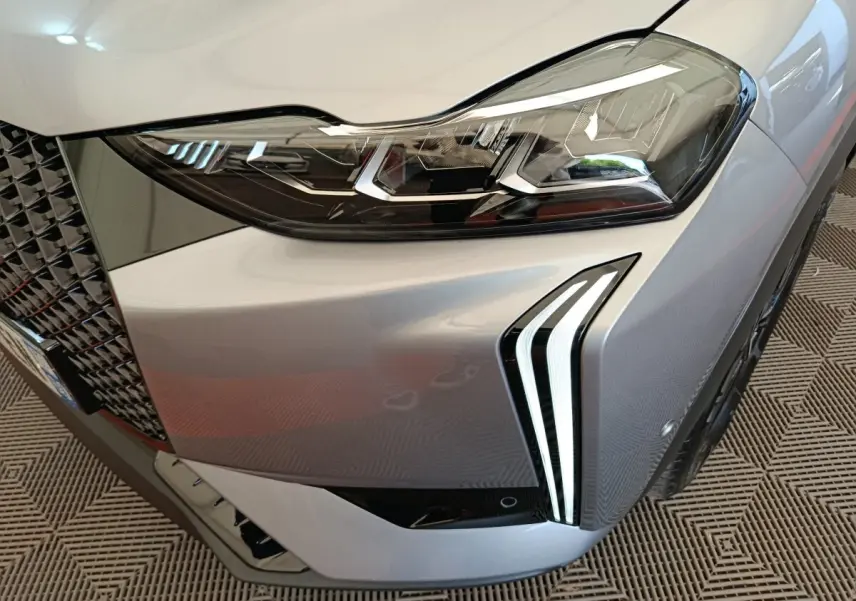 Gros plan sur le phare avant droit gris foncé du DS3 2024 avec signature lumineuse LED distinctive et calandre texturée.