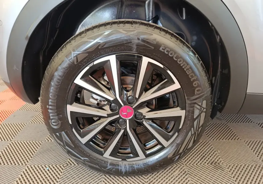 Gros plan sur la roue avant droite du DS3 2024 gris foncé avec jante alliage noire et argentée au logo rose.
