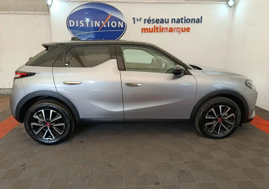 Vue latérale droite d'un DS3 2024 gris foncé avec toit noir et jantes alliage noires, en intérieur showroom.