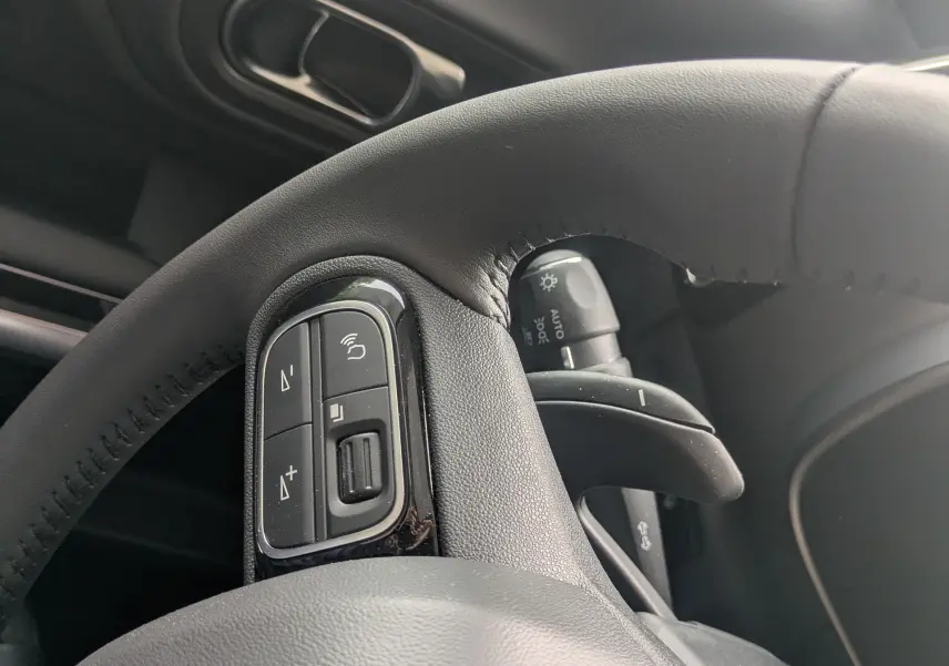 Gros plan sur le volant en cuir noir du Citroën C5 Aircross hybride 2025, avec commandes intégrées et poignée de porte grise visible.