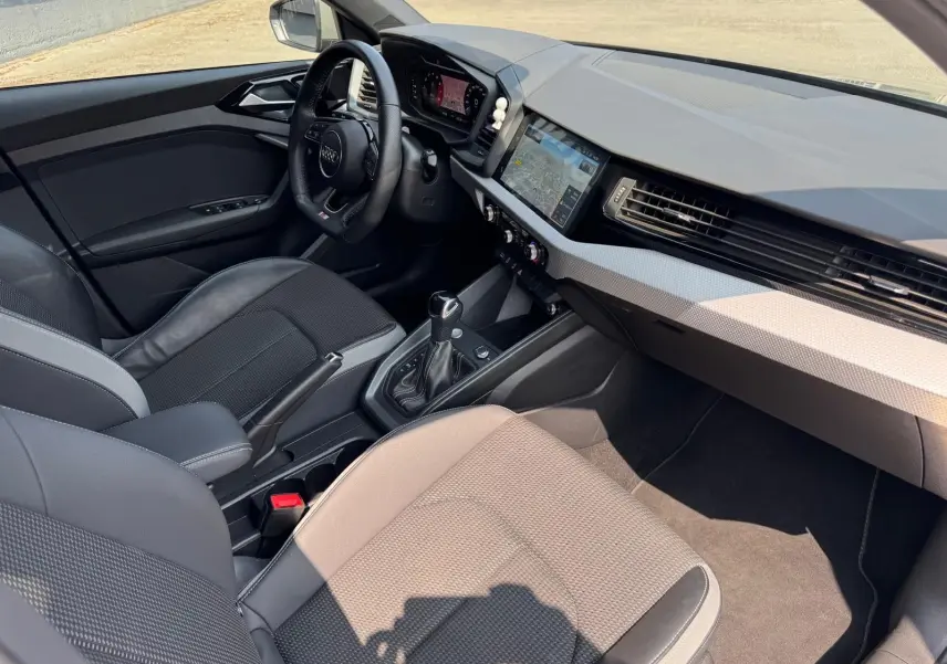 Vue intérieure côté conducteur de l'Audi A1 Sportback gris avec tableau de bord moderne et écran tactile GPS.