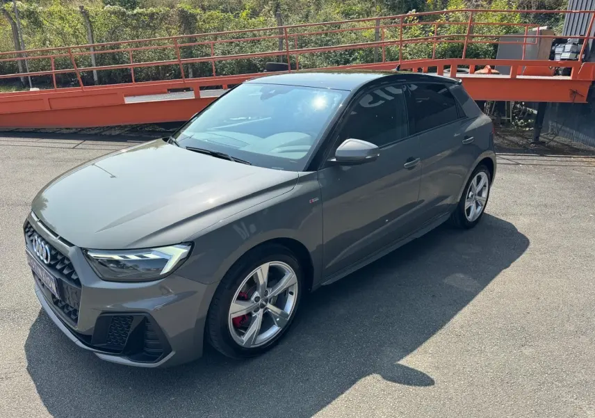 Audi A1 Sportback gris en 3/4 avant droit, avec jantes alliage et étriers de frein rouges visibles.