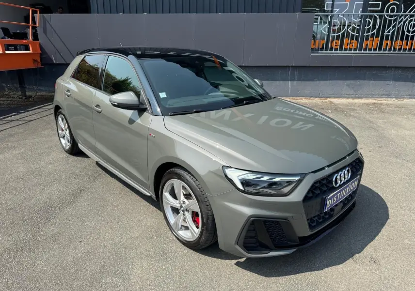 Audi A1 Sportback gris en 3/4 avant droit, avec toit noir et jantes alliage sport S-Line visibles.