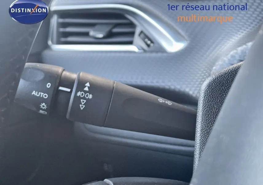 Détail intérieur du commodo d'éclairage à gauche sur Peugeot 2008 gris platinium métal, avec texture de porte visible.