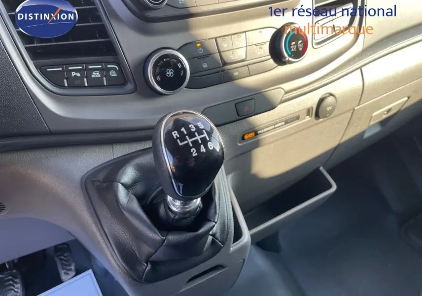 Gros plan sur le levier de vitesses manuel noir du Ford Transit Fourgon blanc, avec tableau de bord et commandes visibles.