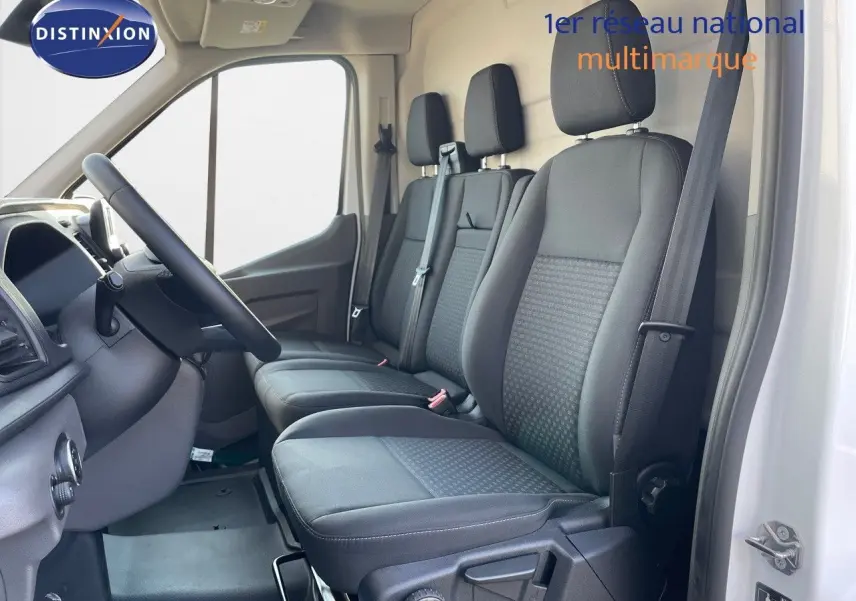 Vue intérieure côté conducteur du Ford Transit Fourgon blanc 2023, montrant les sièges avant en tissu noir et le volant.