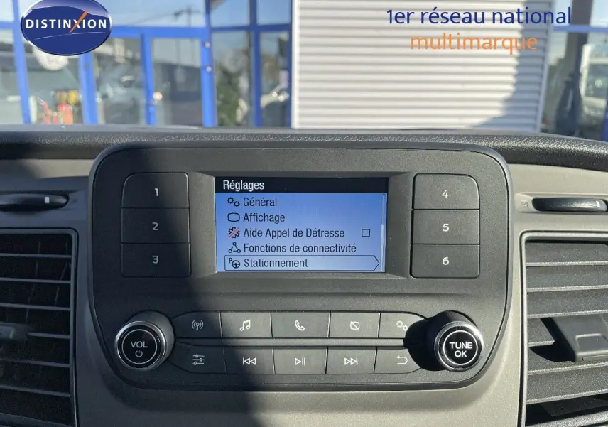 Vue rapprochée de l’écran central du tableau de bord du Ford Transit Fourgon blanc, affichant les réglages.
