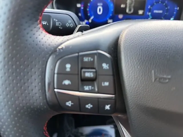 Gros plan sur les commandes au volant à gauche du Ford Focus 1.5 EcoBoost bleu 2022, avec tableau de bord numérique en arrière-plan.