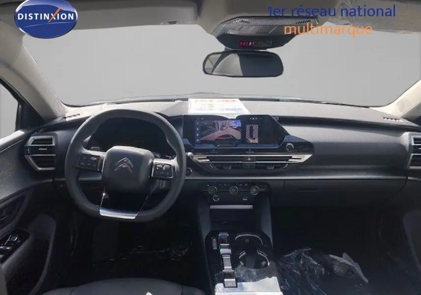 Vue intérieure avant du Citroën C5 X 2023, tableau de bord et volant noir avec écran central tactile allumé.