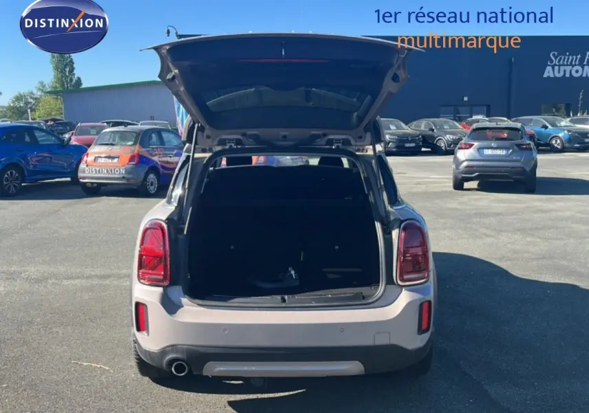Vue arrière d'une MINI Countryman Cooper grise avec coffre ouvert sur un parking ensoleillé.