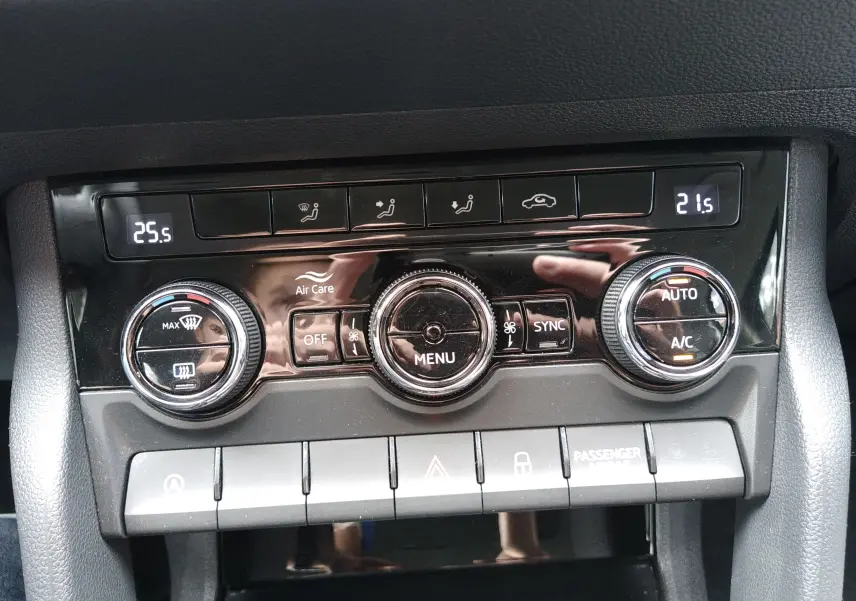 Gros plan sur la console de climatisation du Skoda Karoq gris, avec réglages digitaux et boutons rotatifs visibles.