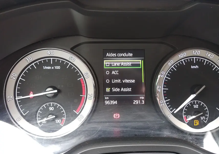 Vue rapprochée du tableau de bord gris du Skoda Karoq 2021, affichant les aides à la conduite et compteurs analogiques.