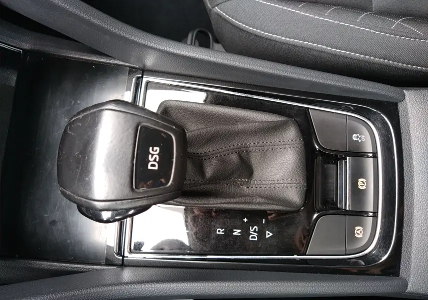 Gros plan sur le levier de vitesses DSG noir brillant du Skoda Karoq gris, avec boutons de contrôle et coutures visibles.
