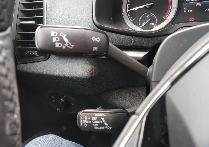 Gros plan intérieur sur les commandes de clignotants et régulateur du Skoda Karoq gris, tableau de bord partiellement visible.