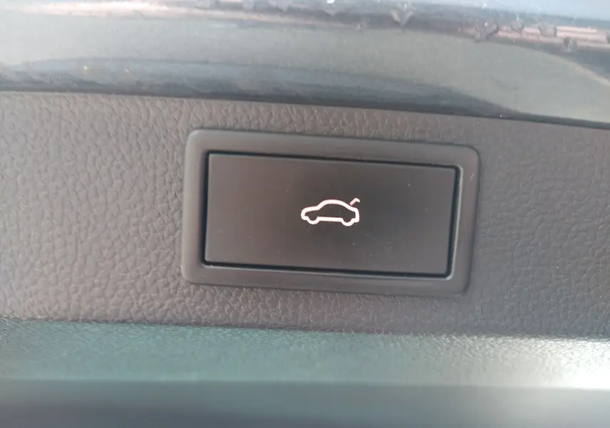 Bouton intérieur noir avec symbole lumineux blanc d'ouverture de coffre, sur Skoda Karoq gris, vue rapprochée du tableau de bord.