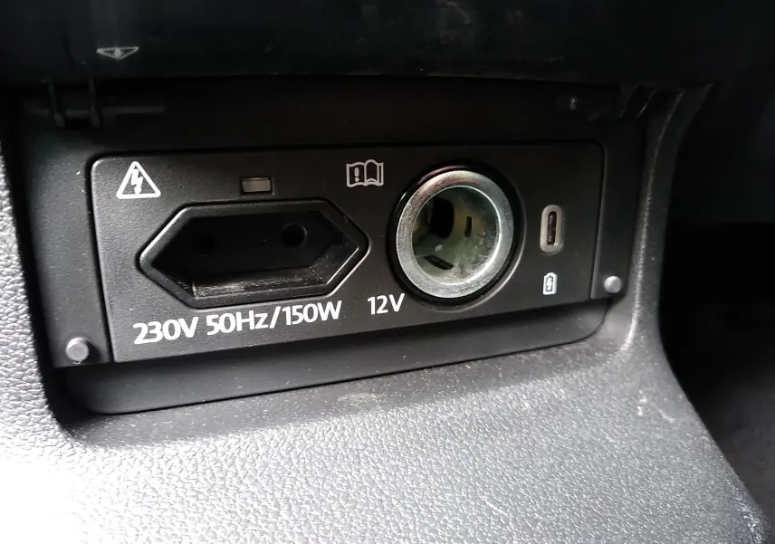 Gros plan sur la prise 230V et l'allume-cigare 12V du tableau de bord intérieur d'un Skoda Karoq gris.