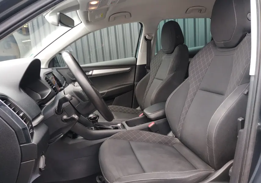 Vue intérieure côté conducteur du Skoda Karoq gris 2021, sièges tissu noir avec surpiqûres contrastées.