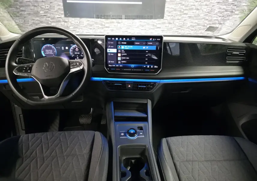 Vue intérieure avant du Volkswagen Tiguan 2025 noir, tableau de bord numérique avec éclairage d'ambiance bleu.